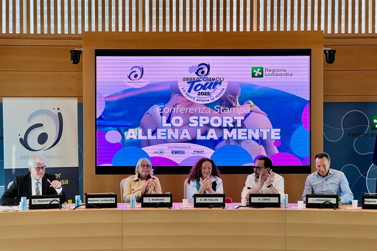 Relatori della conferenza stampa del Tour Abbracciamoli 2025 seduti davanti a un maxi schermo con il logo dell’evento e lo slogan “Lo sport allena la mente”, presso la sede della Regione Lombardia.