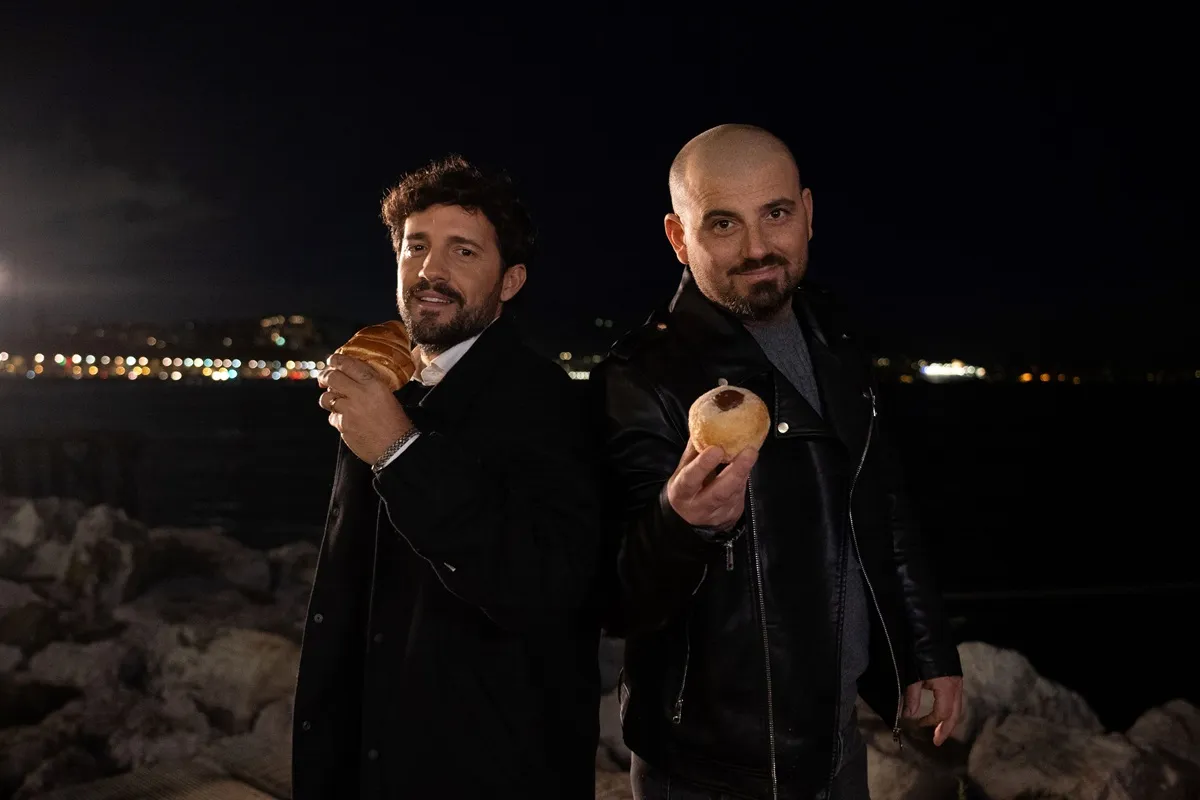 Fabio Esposito e Rocco Cannavino posano di notte sul lungomare, mostrando dolci artigianali tipici della tradizione napoletana.