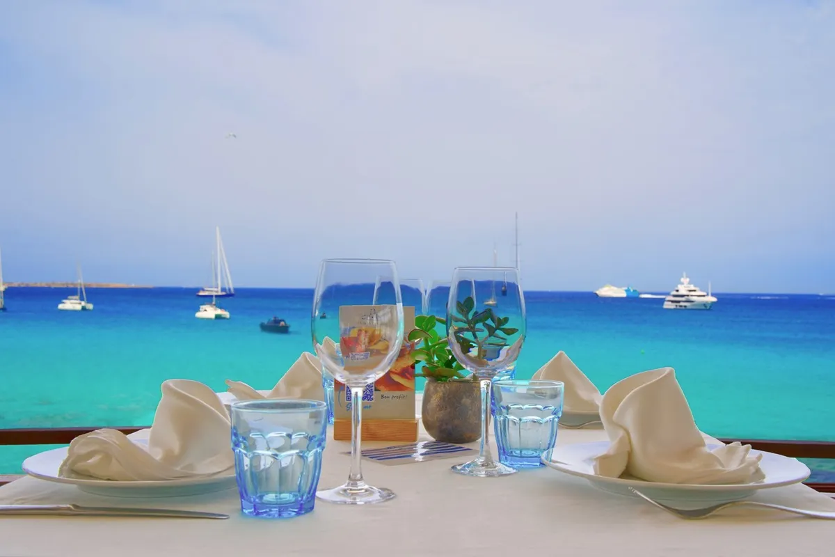 Tavolo apparecchiato con vista sul mare turchese di Formentera e barche all’ancora