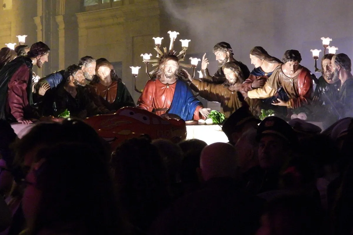 Escultura iluminada da Última Ceia durante a procissão da Quinta-feira Santa em Caltanissetta, com figuras detalhadas de Jesus e os apóstolos, rodeadas por espectadores à noite.