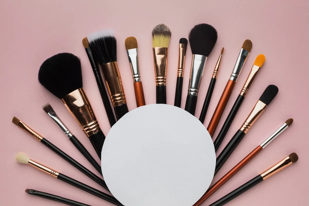 Pennelli da trucco disposti a semicerchio su sfondo rosa con spazio centrale bianco per testo o logo