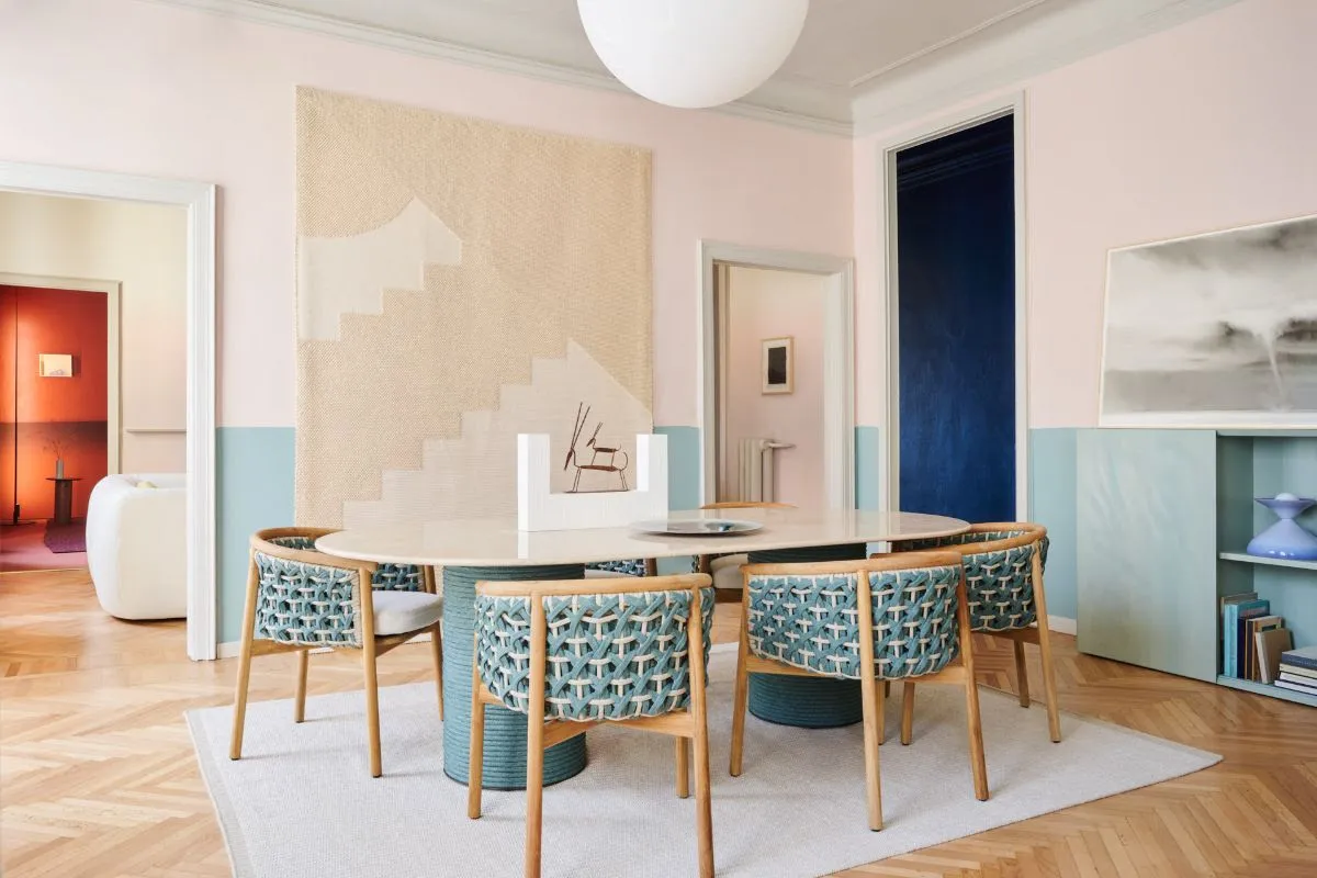 Sala de jantar com mesa oval, cadeiras artesanais de madeira e palha azul, piso em espinha de peixe e elementos de design contemporâneo no Brera Design Apartment.