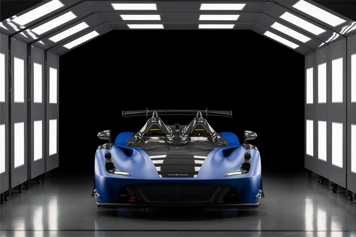 La Dallara Stradale, una supercar in stile racing, esposta in una sala di verniciatura con illuminazione intensa. La carrozzeria blu metallica e i dettagli neri si evidenziano contro il fondo nero.