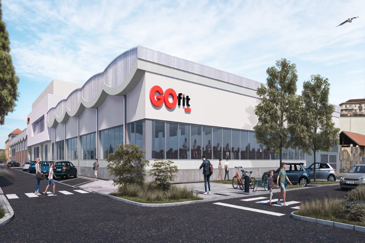 Renderização 3D da fachada do novo centro GO Fit em Turim, com logo em vermelho, janelas amplas e um ambiente urbano moderno, incluindo árvores e veículos estacionados.