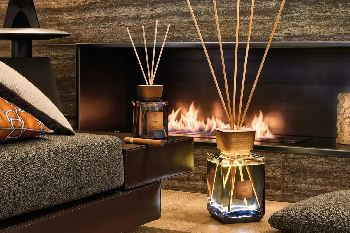 Diffusore di fragranza Locherber Milano in un ambiente elegante con camino, scelte di arredo moderne e un flacone in vetro con tappo in legno. Il diffusore è posizionato su un tavolino accanto a un divano, mentre il fuoco sullo sfondo aggiunge un'atmosfera calda e accogliente.