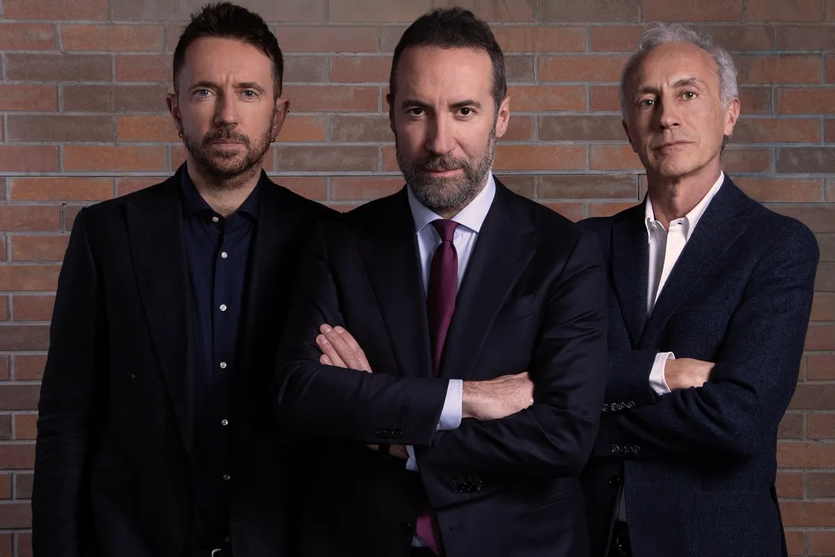 I conduttori di Accordi & Disaccordi: Andrea Scanzi, Luca Sommi e Marco Travaglio in posa davanti a un muro di mattoni, pronti per il dibattito politico su Discovery+
