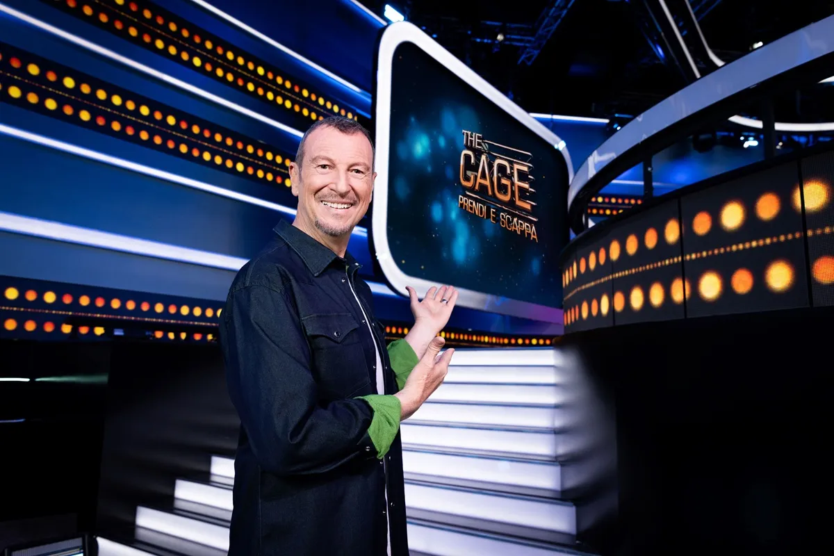 Immagine di Amadeus, conduttore del programma 'The Cage: Prendi e Scappa', mentre presenta il logo del programma in un set televisivo moderno