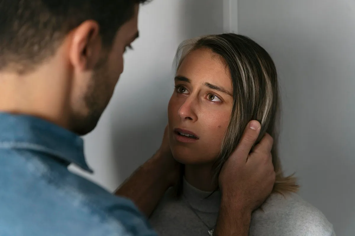 Immagine di una coppia in un momento di tensione emotiva, con un uomo che tiene la testa di una donna, mentre lei lo guarda con preoccupazione. La scena simboleggia un conflitto emotivo e una dinamica di dipendenza affettiva.