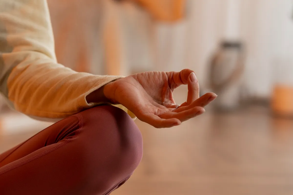 Immagine di una mano in posizione di mudra durante una sessione di meditazione, con una persona seduta in posizione di loto