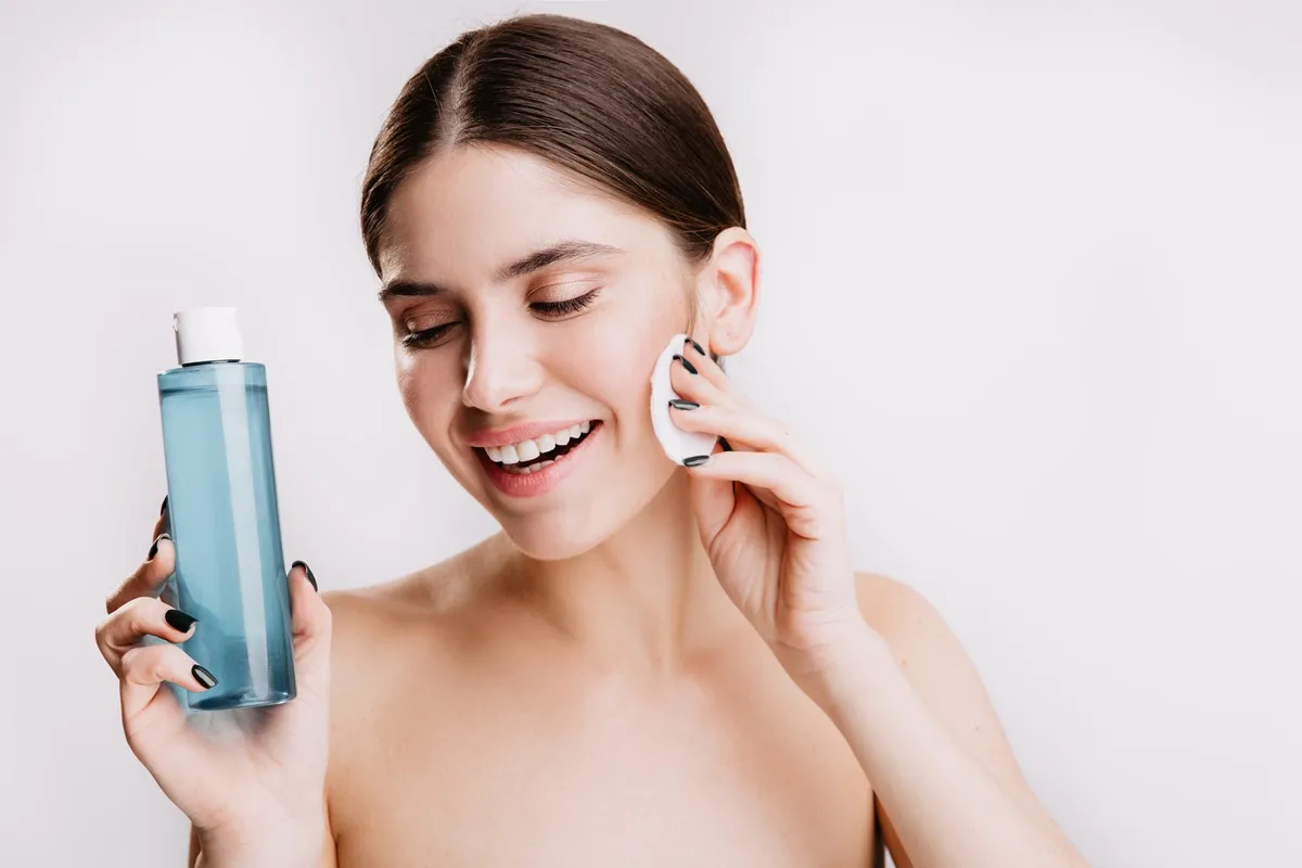 Donna sorridente che applica il tonico viso con un dischetto di cotone, mostrando il prodotto in mano