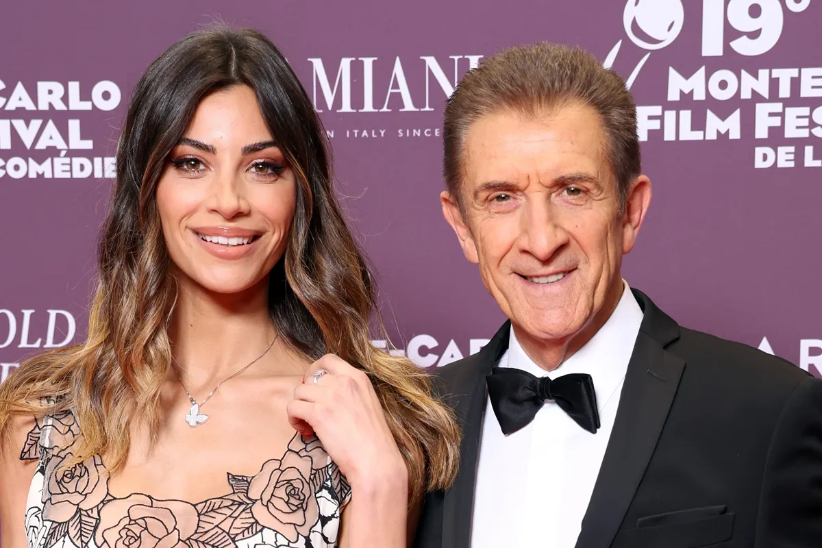 Coppia sorridente insieme sul tappeto rosso del Festival di Cinema di Monaco. Lei indossa un elegante vestito con disegni floreali, mentre lui è in abito nero con papillon