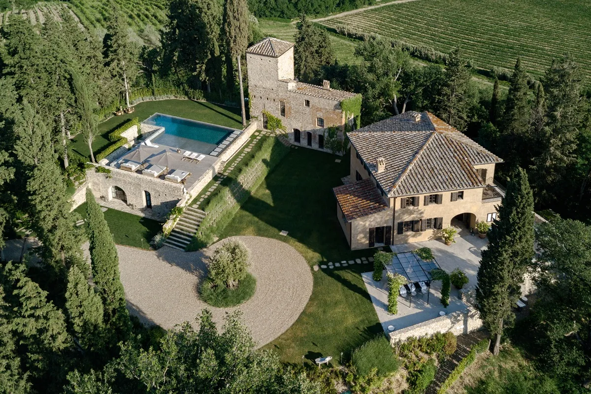 Vista aerea di una proprietà medievale in Toscana con piscina, giardini ben curati e una villa elegante circondata da vigneti e alberi verdi.