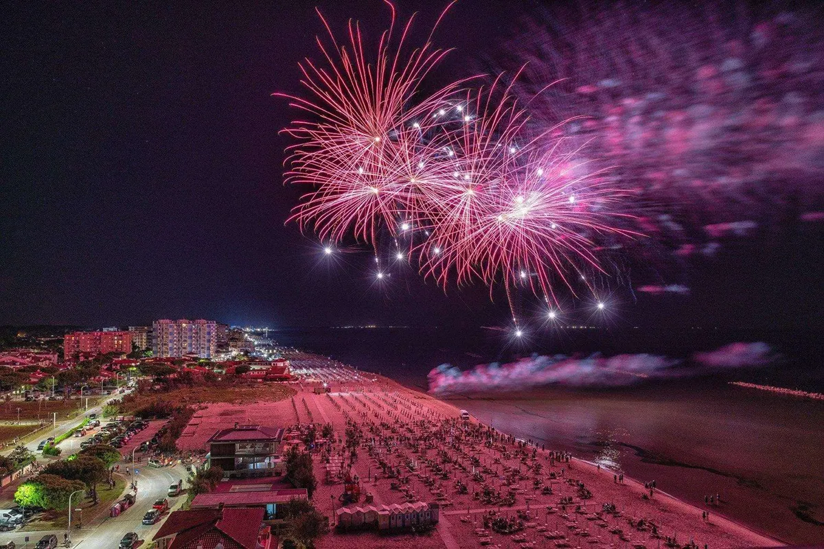 Fuochi d’artificio rosa esplodono nel cielo notturno sopra la spiaggia di Rimini illuminata dalla “Notte Rosa”.