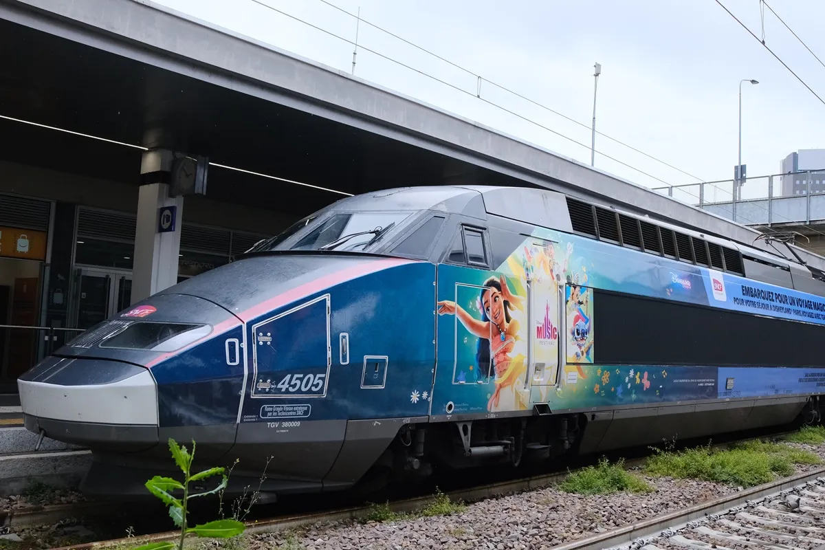 Immagine del TGV INOUI decorato con temi Disney, con un primo piano del personaggio Moana e il logo del Disney Music Festival, fermo in una stazione ferroviaria.