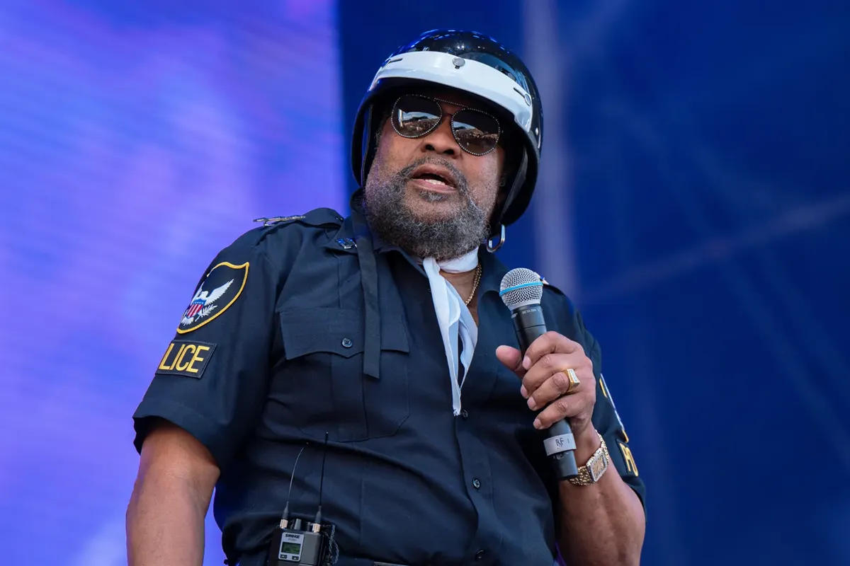 Victor Willis, cantante dei Village People, con uniforme da poliziotto e microfono in mano durante un’esibizione sul palco