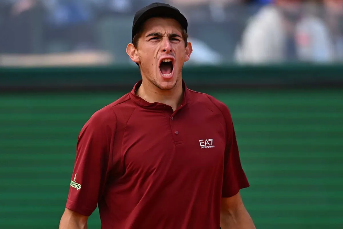 Matteo Arnaldi grida in campo durante una partita di tennis sull’erba, indossando una maglietta EA7 bordeaux