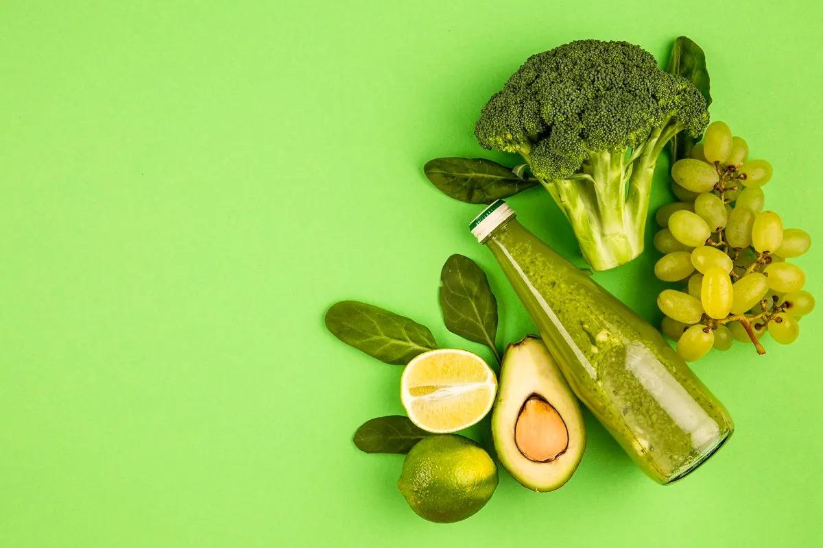 Immagine di ingredienti freschi per una dieta detox, inclusi broccolo, uva, avocado, lime e una bottiglia di frullato verde