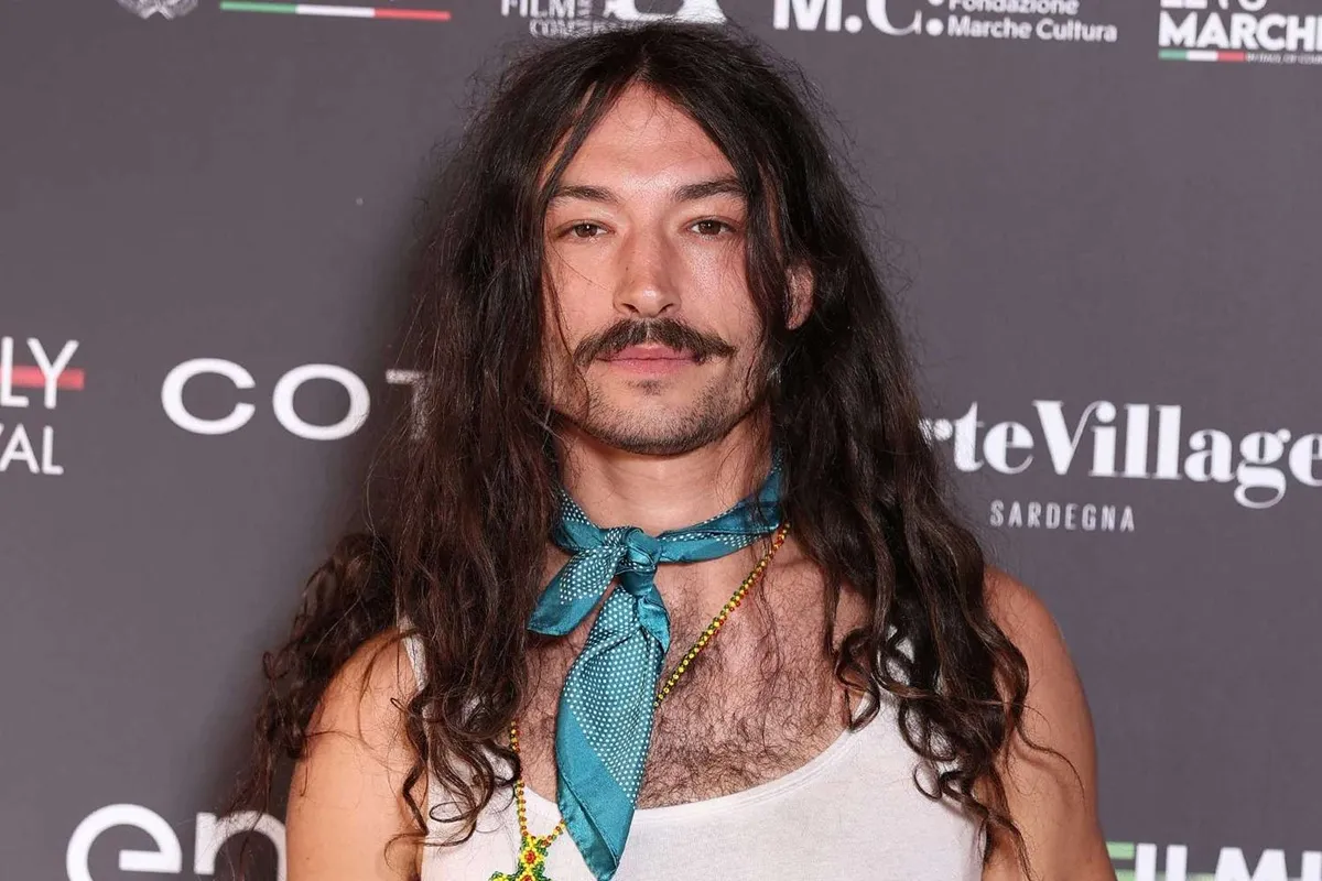 Ezra Miller con capelli lunghi, baffi e foulard azzurro al collo durante il Filming Italy Festival 2025