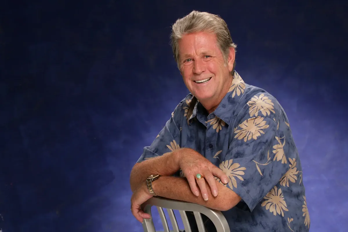 Brian Wilson, il famoso musicista dei Beach Boys, sorride indossando una camicia hawaiana con fiori grandi, posando per una foto professionale