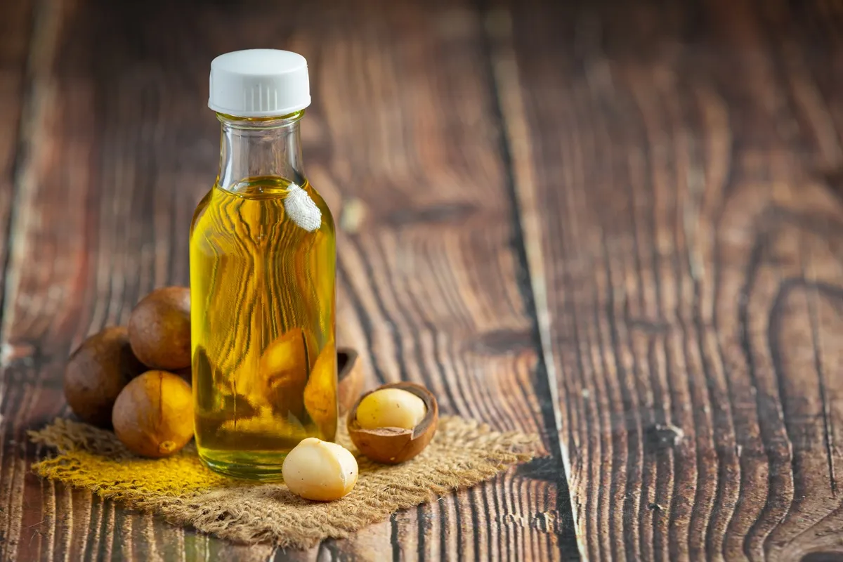 Bottiglia trasparente di olio di argan con tappi bianchi accanto a noci di argan su superficie in legno rustico