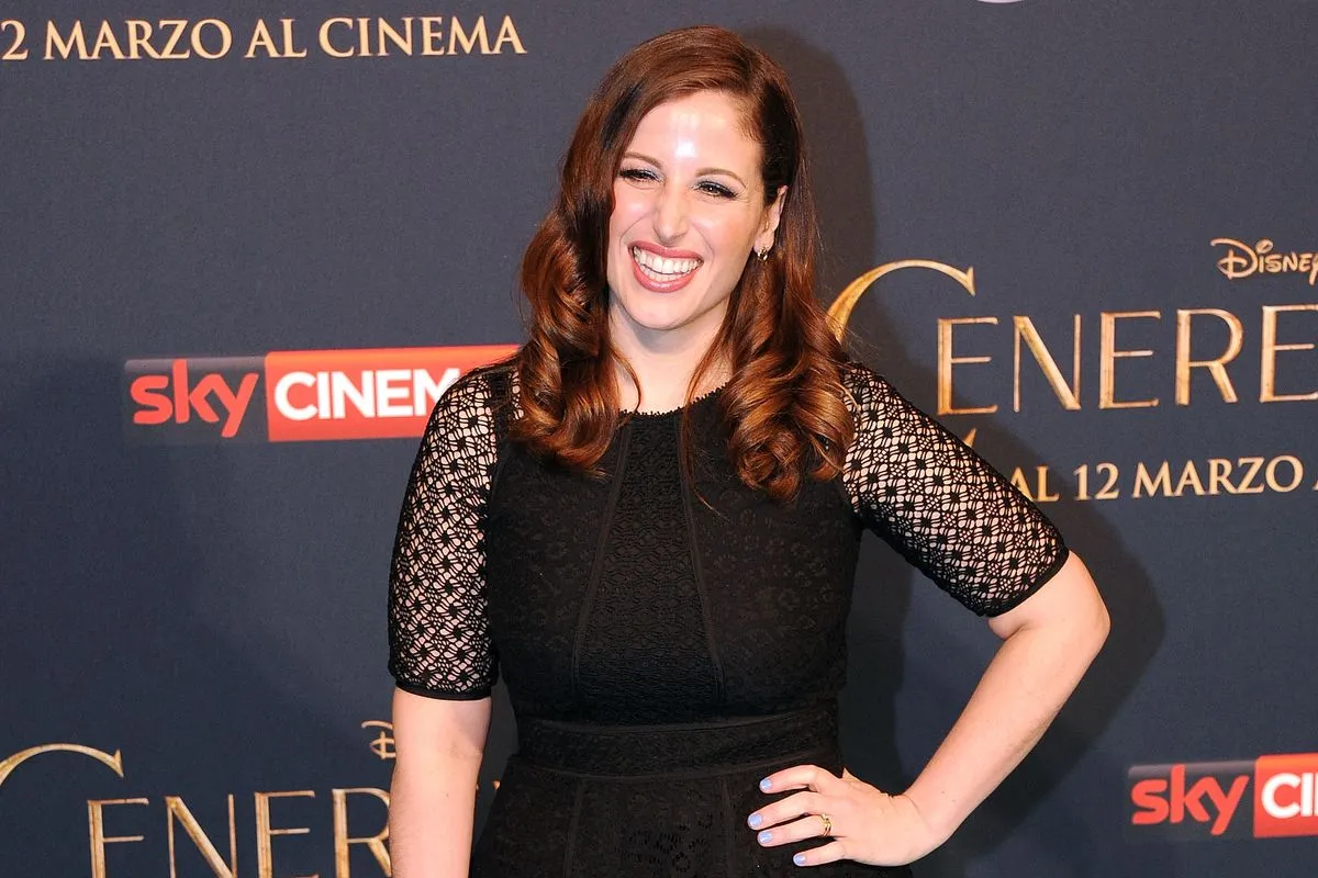 Clio Zammatteo sorride con eleganza indossando un abito nero a maniche in pizzo, durante un evento promozionale Disney a marzo, davanti a un backdrop con i loghi Sky Cinema e Cenerentola.