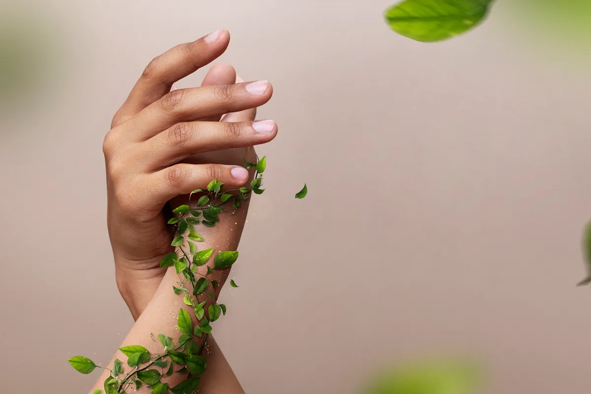 Due mani femminili avvolte da piccole foglie verdi su sfondo neutro, simbolo di bellezza naturale cruelty free