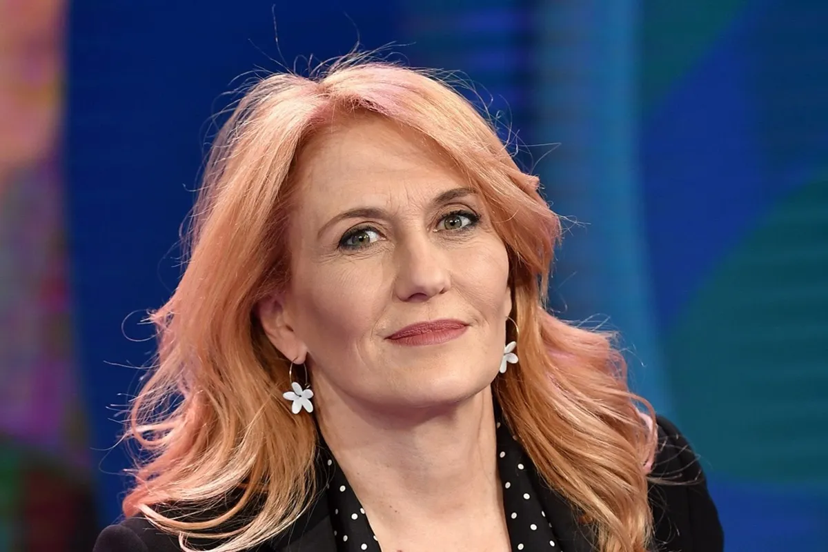 Ritratto di una donna con capelli biondo ramato, indossa orecchini bianchi a forma di fiore e un abito nero a pois.