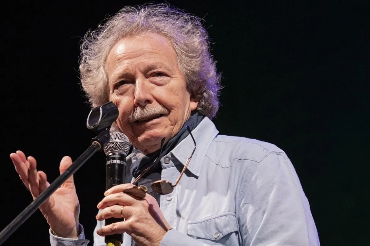 Fabio Concato canta dal vivo tenendo un microfono, con espressione intensa e camicia chiara, durante una performance sul palco.