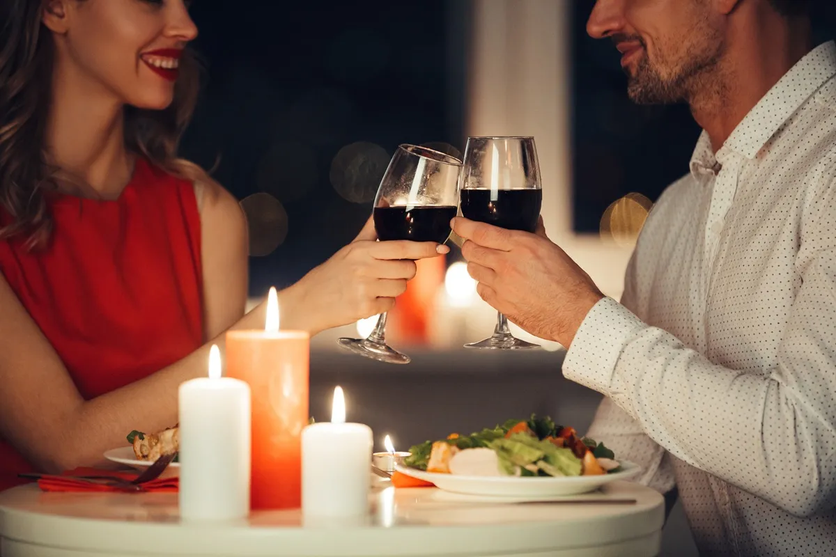 Coppia che brinda con due calici di vino rosso a una cena romantica illuminata da candele sul tavolo