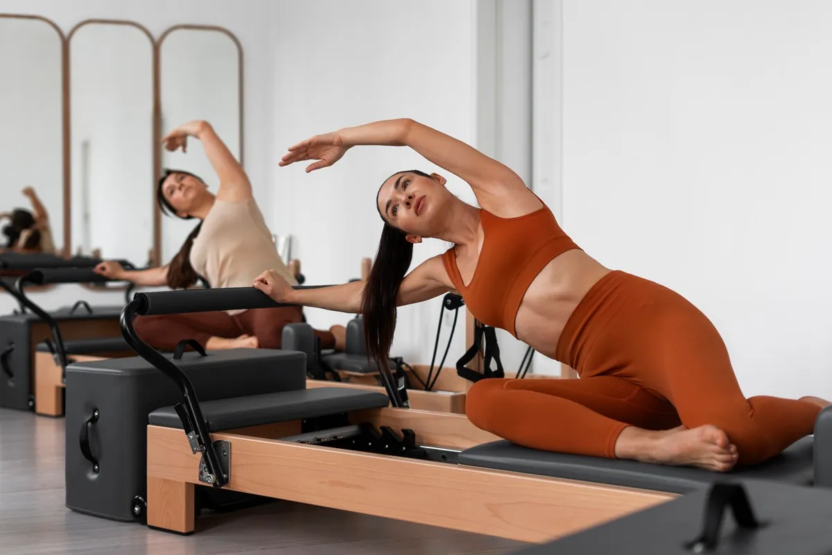 Due donne praticano Pilates Reformer eseguendo esercizi di allungamento laterale in una sala fitness moderna