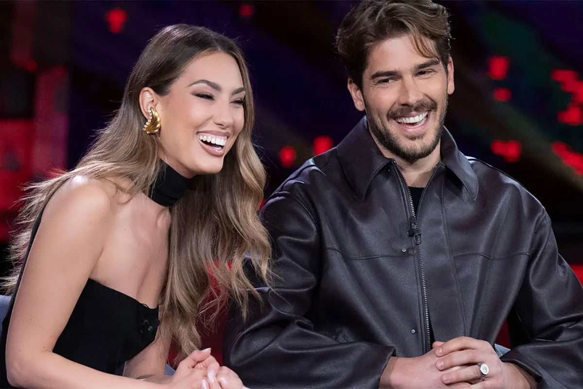 Donna e uomo sorridenti in studio televisivo, seduti fianco a fianco, mentre annunciano la data del loro matrimonio.