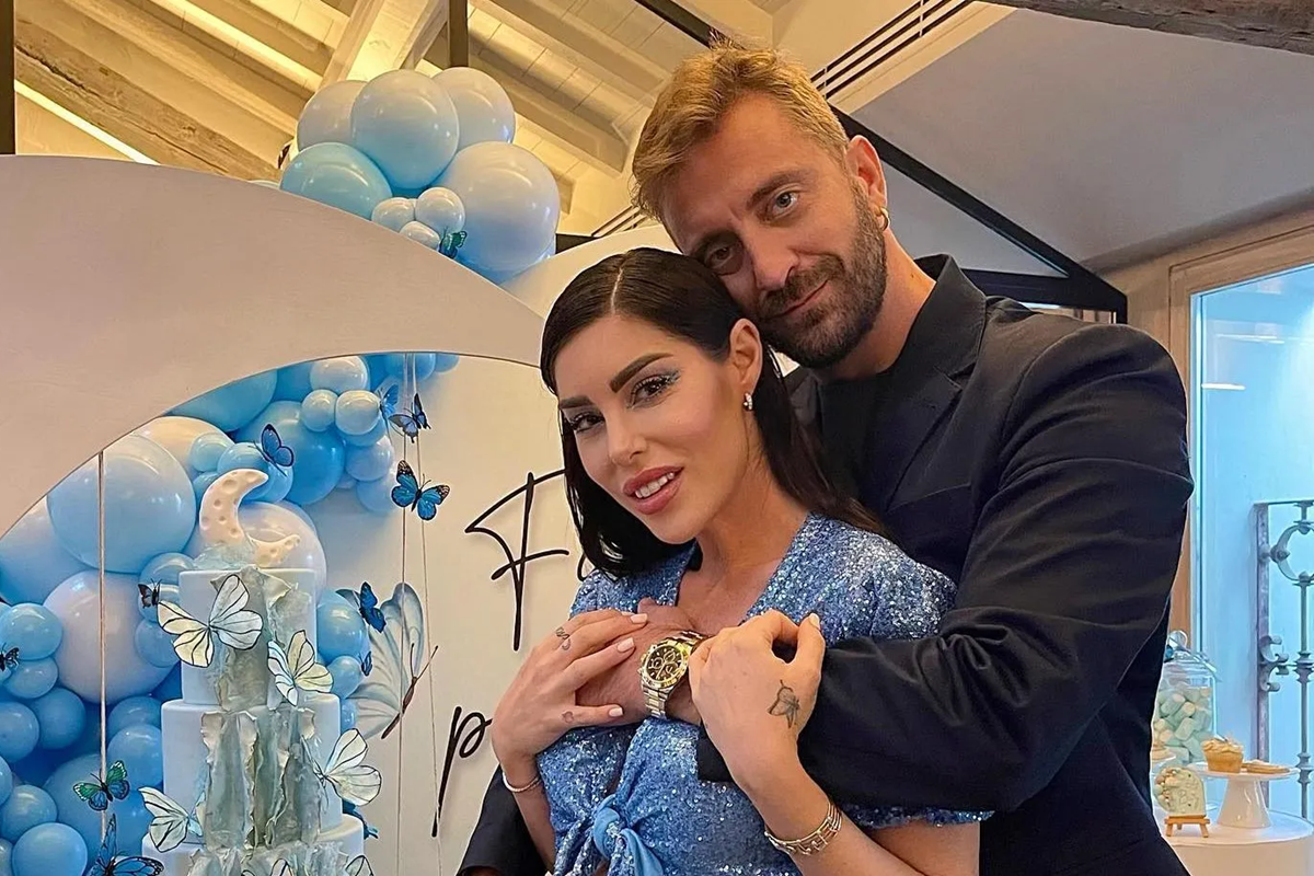 Stefano Corti abbraccia Bianca Atzei durante un evento privato con decorazioni blu e torta a tema farfalle
