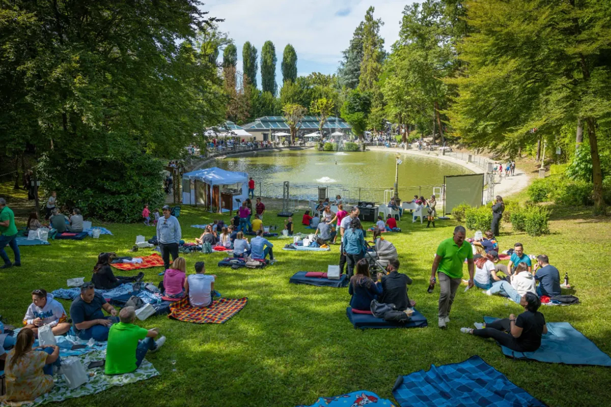 Persone sedute su coperte colorate che fanno picnic sul prato accanto al lago durante il Festival della Vendemmia di Fontanafredda al Villaggio Narrante