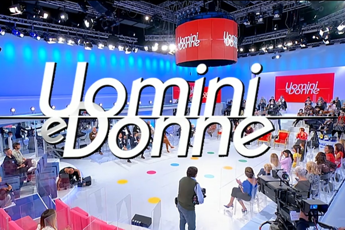 Studio televisivo di Uomini e Donne, con pubblico, telecamere e schermi luminosi che mostrano il logo del programma.