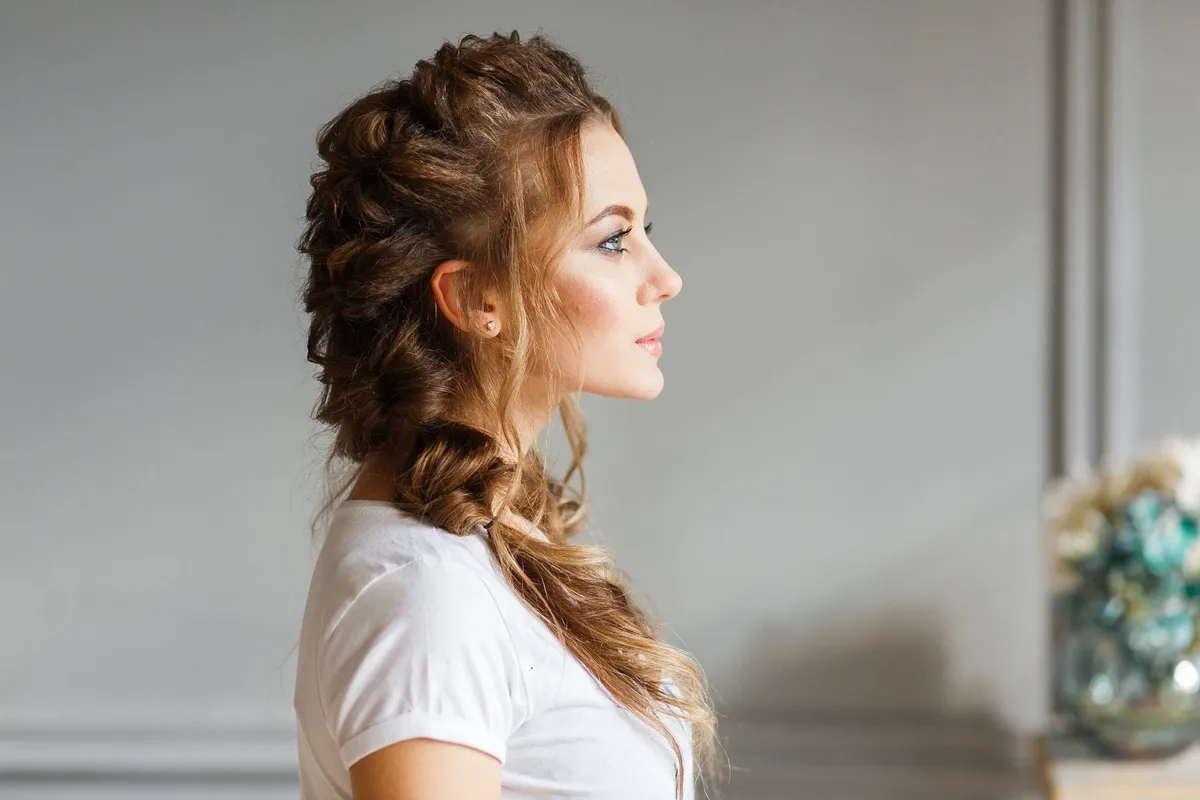 Donna con capelli lunghi e mossi raccolti in una treccia laterale elegante, vista di profilo.