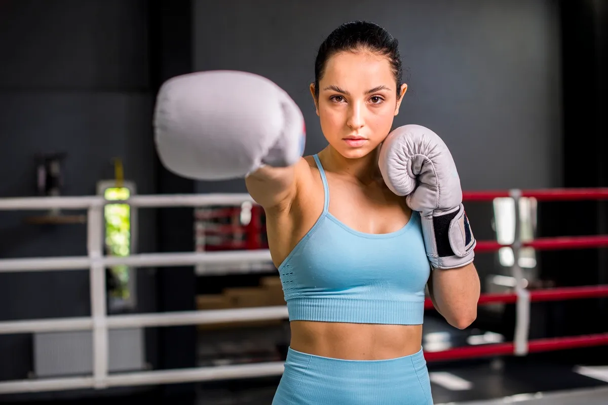 Donna con guantoni da boxe e top sportivo azzurro esegue un pugno diretto durante un allenamento di fit boxe in palestra.