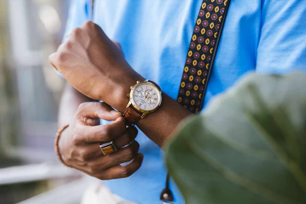Uomo con camicia azzurra e bretella decorata che regola un orologio dorato di lusso con cinturino in pelle marrone al polso