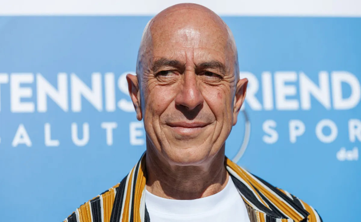 L’attore italiano Roberto Ciufoli sorride davanti a un cartellone blu durante un evento sportivo, dopo aver superato un intervento per cancro renale.