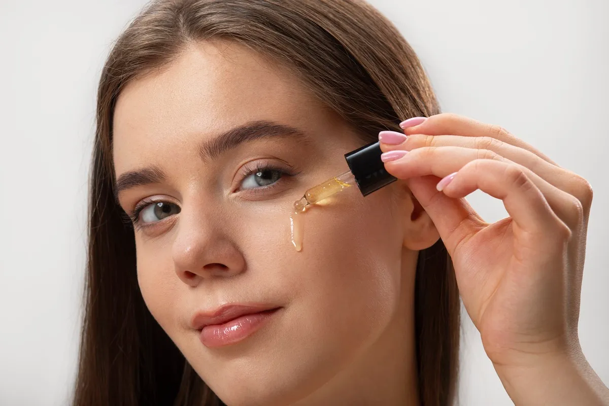 Giovane donna che applica con un contagocce siero alla vitamina C sulla pelle del viso.