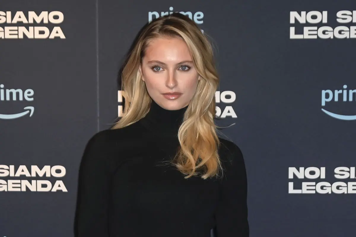 Attrice con capelli biondi e abito nero posa sul red carpet davanti al logo della serie “Noi Siamo Leggenda” durante l’evento di presentazione Prime Video.