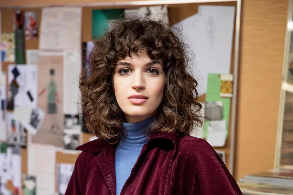 Donna con capelli ricci e giacca bordeaux in ambiente creativo