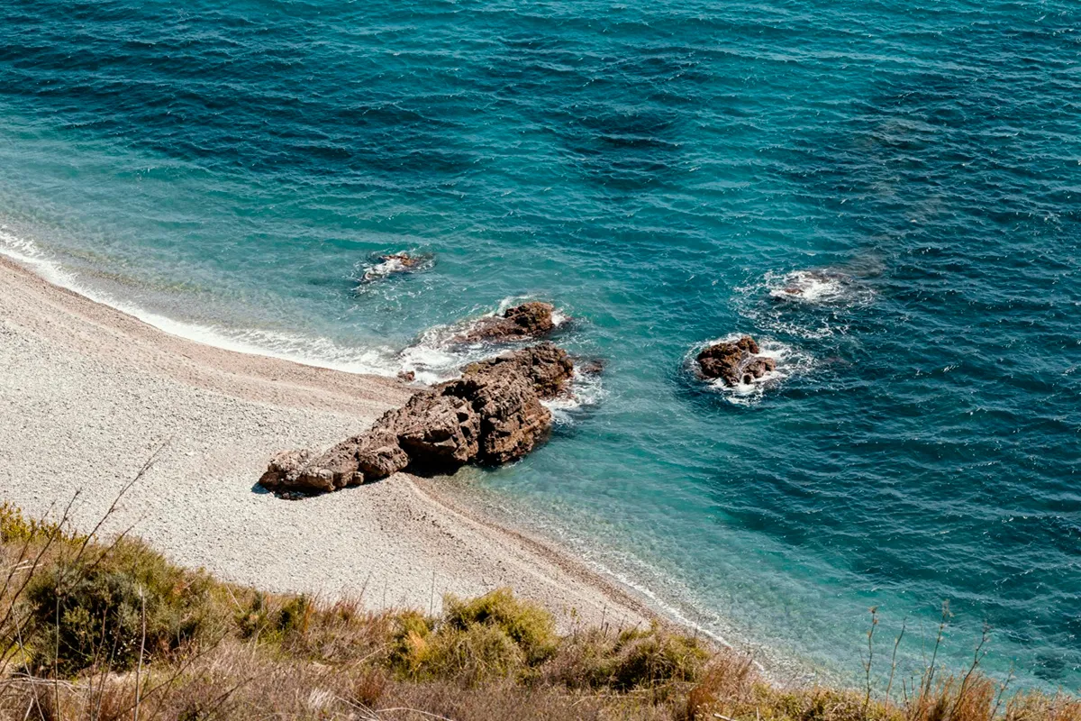 Vista dall’alto di una spiaggia isolata con sabbia chiara, scogli e mare turchese nel sud d’Europa