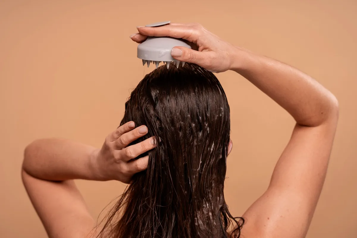 Donna che massaggia il cuoio capelluto con una spazzola in silicone durante il lavaggio dei capelli