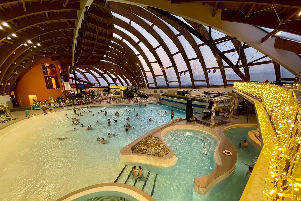 Piscina interna di Acquaworld con cupola in legno, luci calde e visitatori che nuotano in un ambiente tropicale al chiuso.