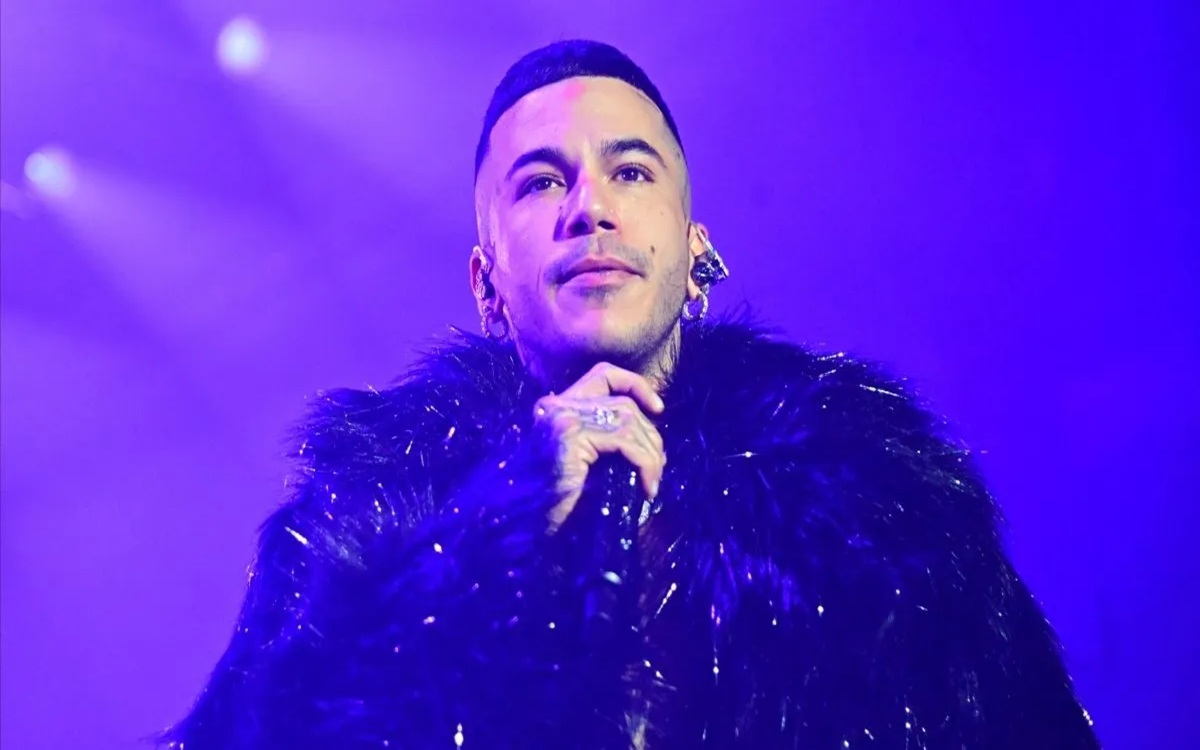 Sfera Ebbasta canta sul palco avvolto in una pelliccia nera sotto luci viola intense.