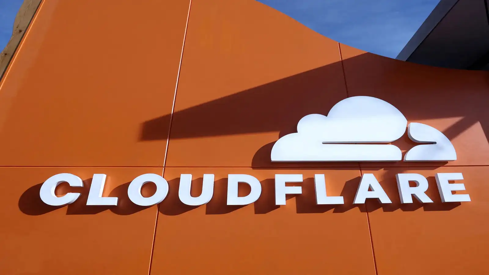 Logo della Cloudflare in bianco su una parete arancione con cielo azzurro sullo sfondo.