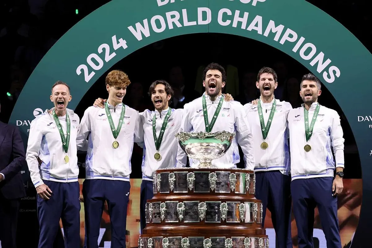 Squadra di tennis festeggia la conquista della Coppa Davis 2024 con trofeo e medaglie.