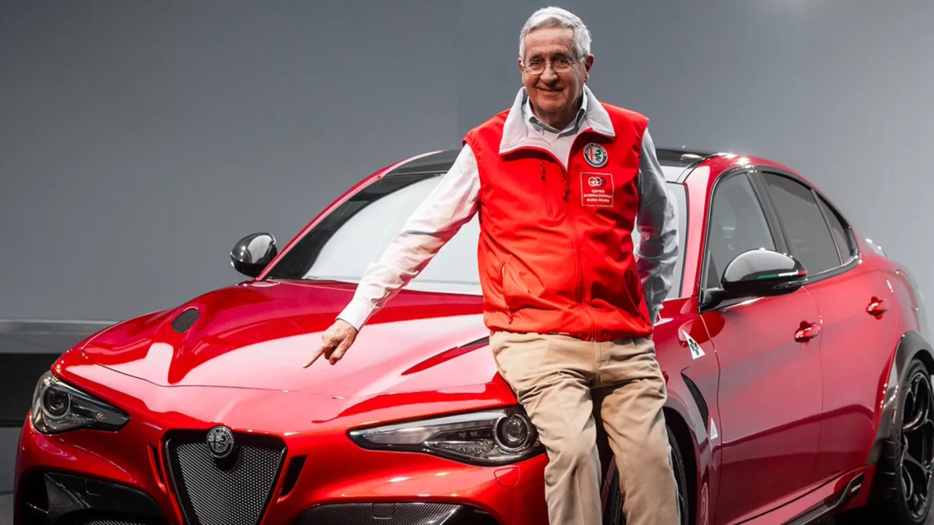 Uomo anziano sorridente accanto a un’Alfa Romeo Giulia GTA rossa, durante una presentazione automobilistica ufficiale.