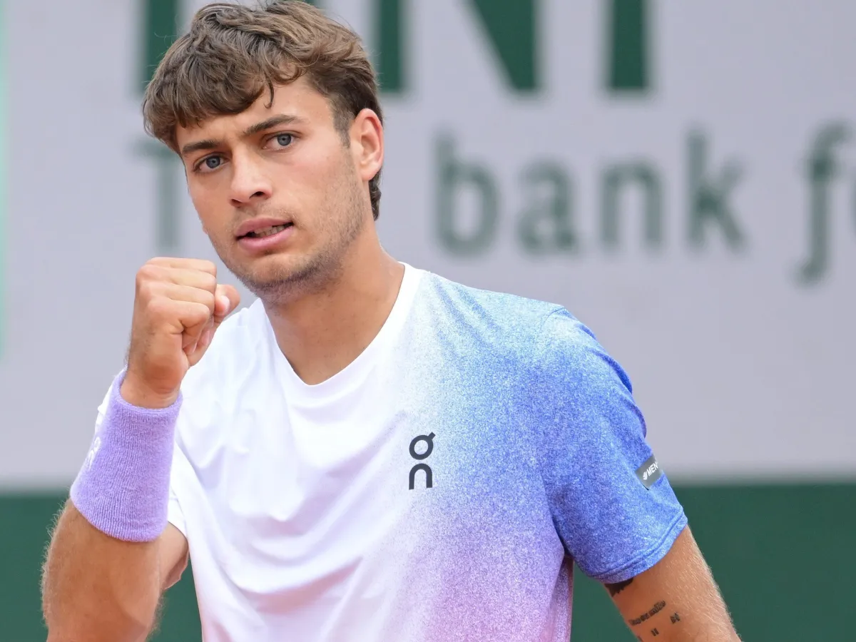 Giocatore di tennis giovane comemora com o punho cerrado durante uma partida, usando camiseta esportiva nas cores branco e azul.