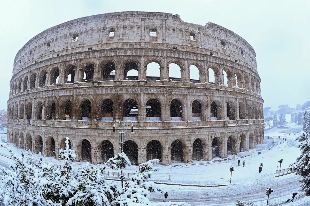 Colosseo di Roma coperto di neve durante una rara nevicata invernale, con strade e alberi completamente brancos.
